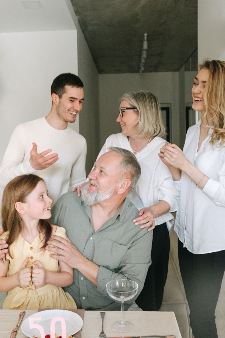 Família de três gerações reunida à mesa, conversando e sorrindo.